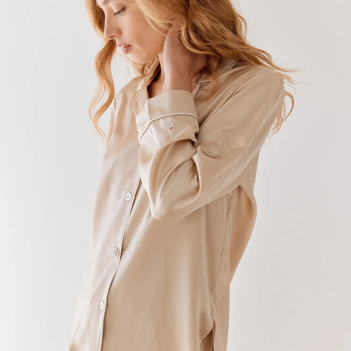 Femme portant une chemise de nuit en soie champagne Maison CÉTOILE, avec passepoil blanc, boutons nacrés et broderie signature sur la manche.