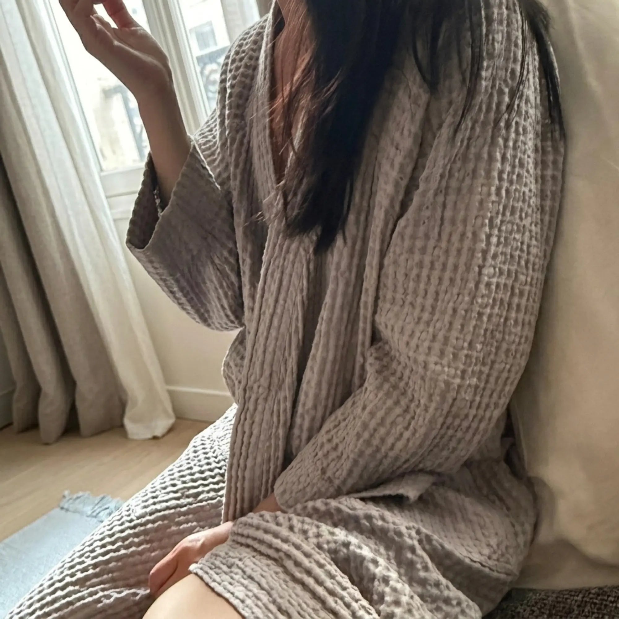 Femme portant un peignoir Waffle en coton gaufré Gris Perle près d’une fenêtre