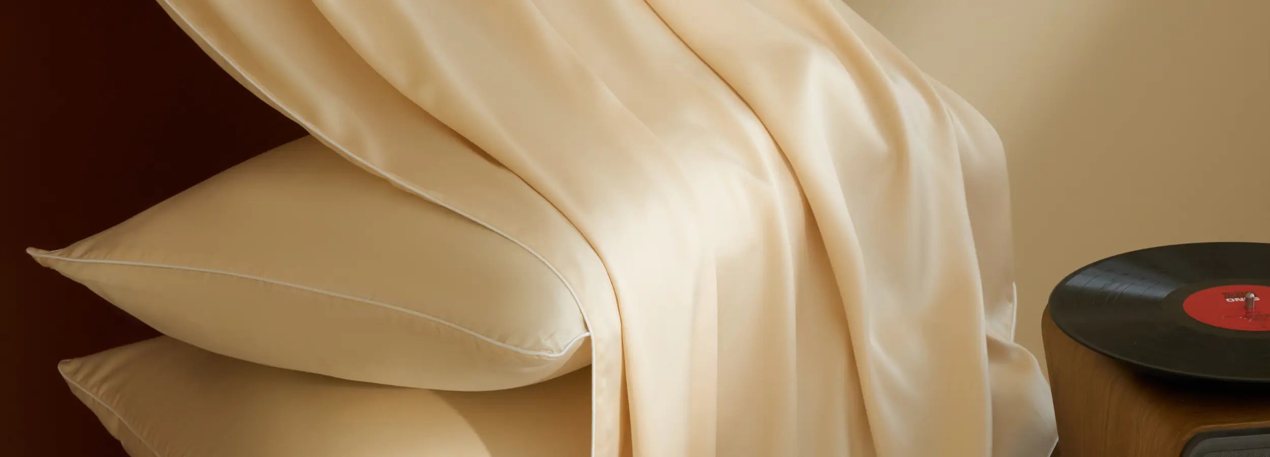 Linge de lit en TENCEL™ Lyocell beige ivoire avec taies d’oreiller assorties, drapé élégant et détail vinyle rouge dans un intérieur chaleureux.