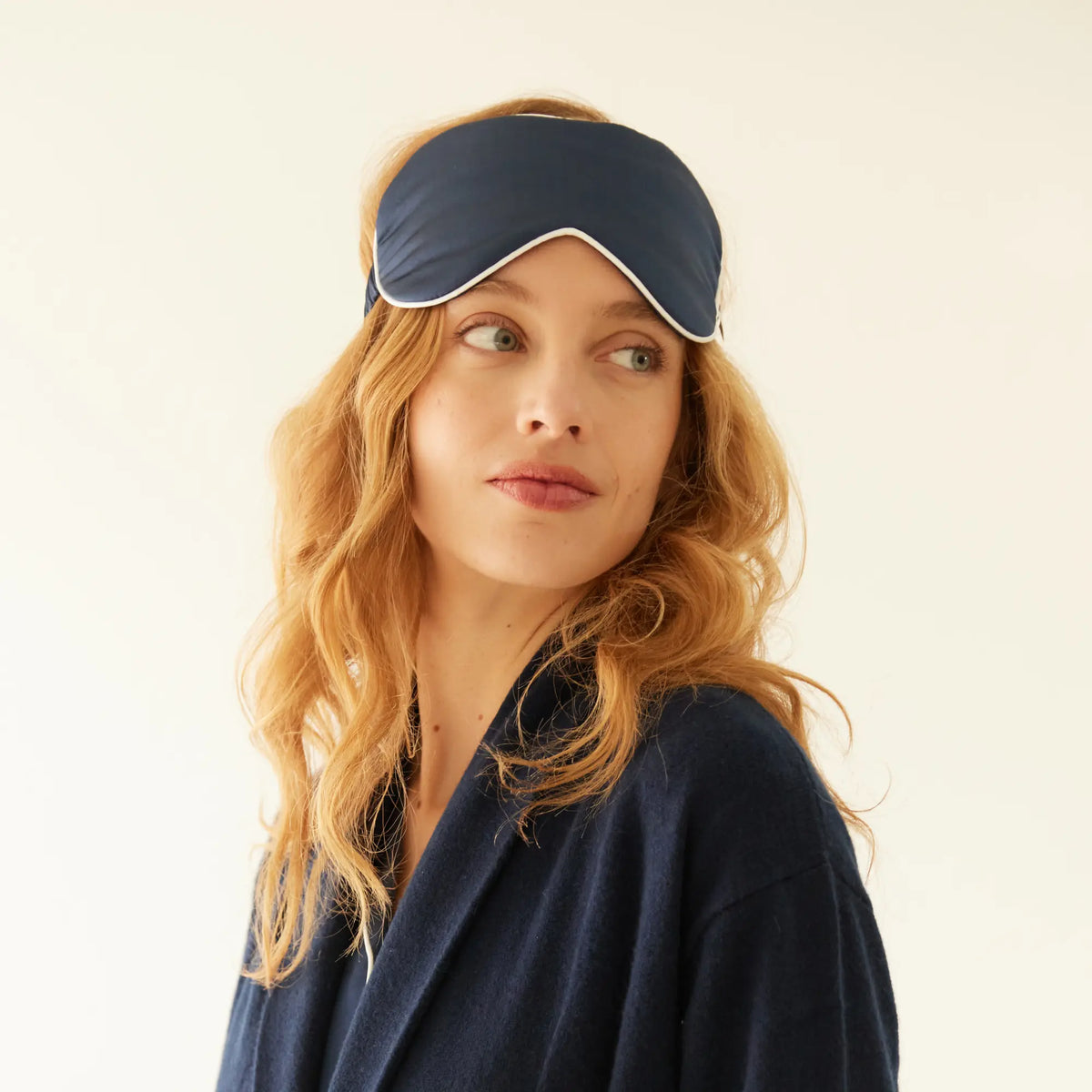 Femme portant un masque de nuit en soie naturelle bleu nuit Maison CÉTOILE, assorti à une tenue d'intérieur bleu marine.