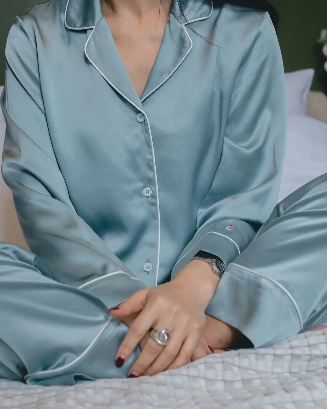Femme portant un pyjama en soie de mûrier bleu grisé Brume d'Été, assise sur un lit, mettant en valeur la douceur et les reflets naturels de la soie.