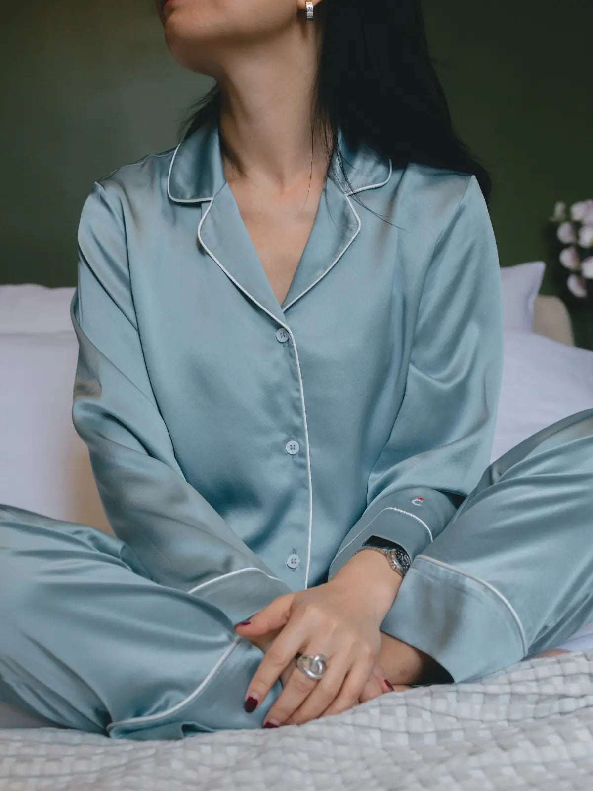 Femme portant un pyjama en soie de mûrier bleu grisé Brume d'Été, assise sur un lit, mettant en valeur la douceur et les reflets naturels de la soie.